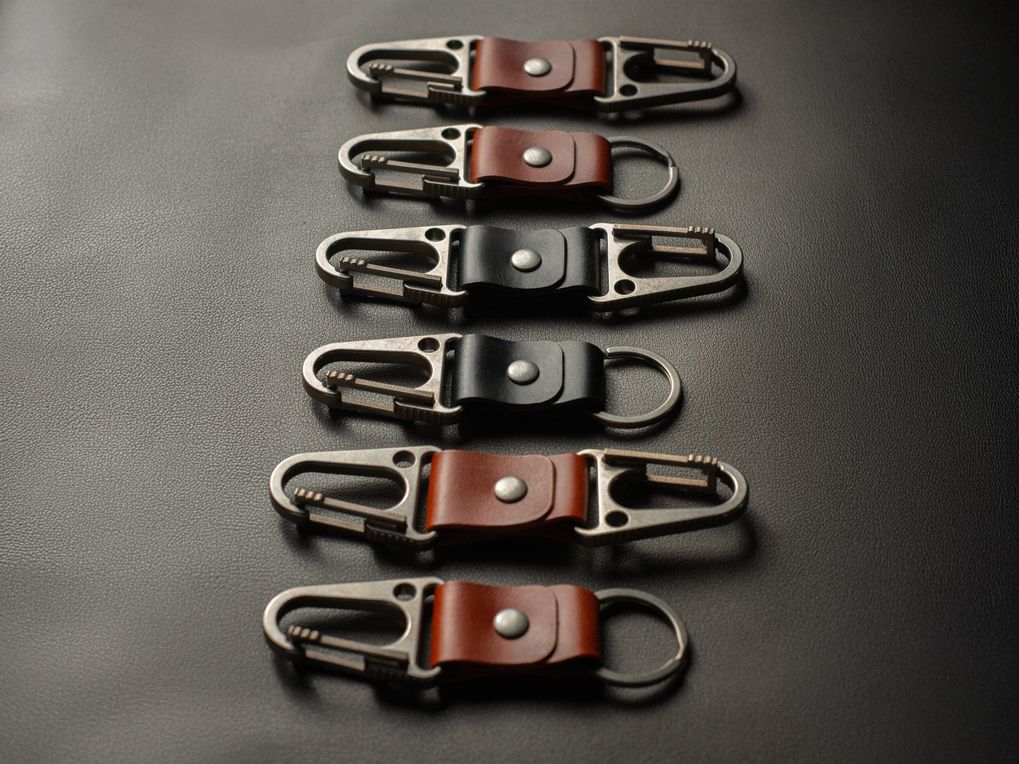 Set of six leather keychains with titanium clasps on a dark surface