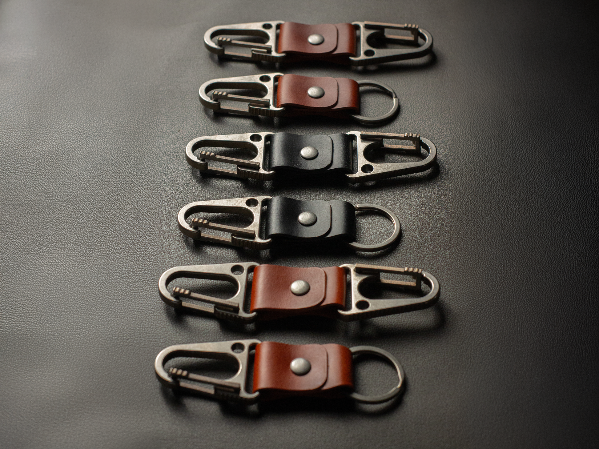 Set of six leather keychains with titanium clasps on a dark surface